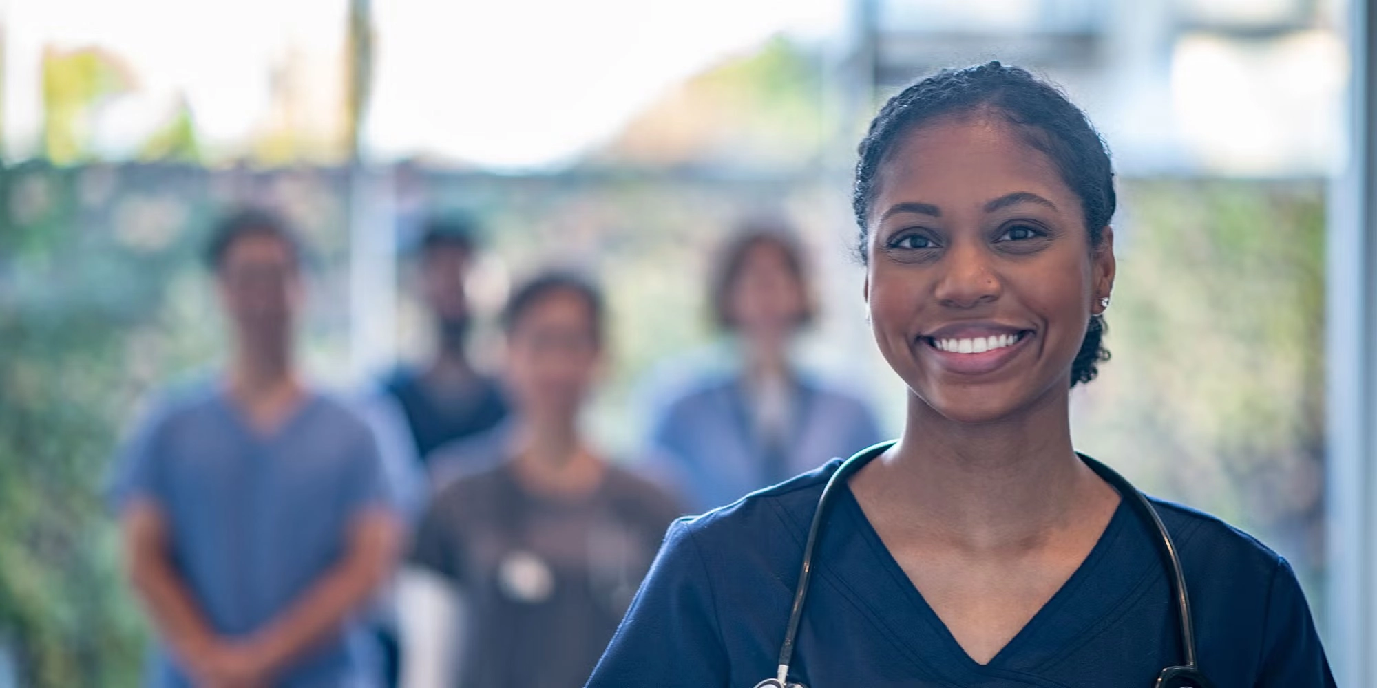 Five medical residents pose together in a hospital hallway. One of the women stands closest to the camera, smiling with her hair pulled back and wearing blue scrubs.