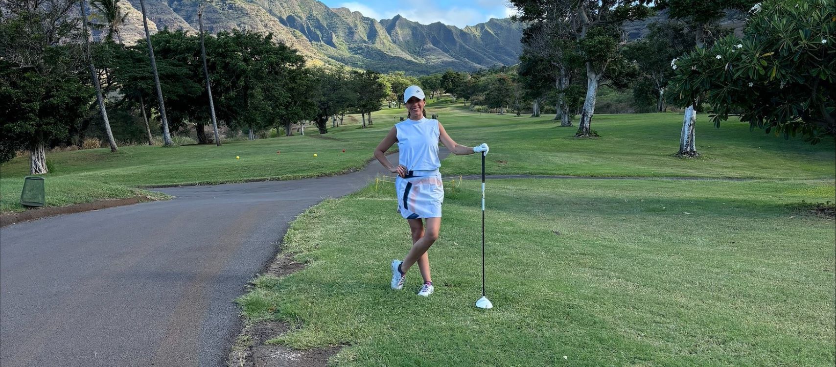 Dana posing on a golf course holding a club in front of mountains