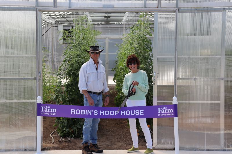 Jim and Robin stand in front of hoop house ready to cut the ribbon