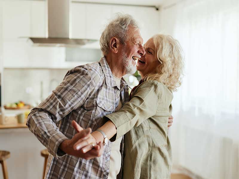An aged couple dances in their kitchen