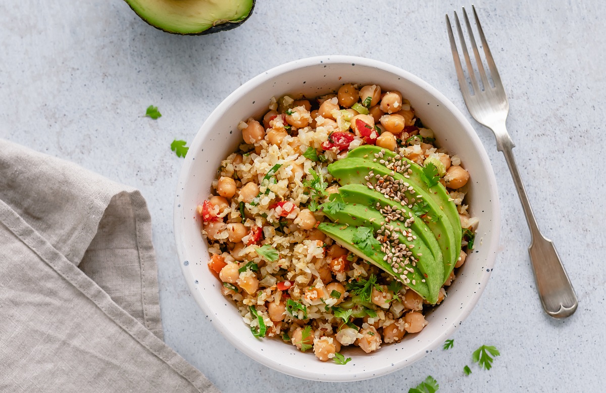 White bowl filled with cooked chickpeas and avocado garnish, sprinkled with sesame seeds and placed on a grey countertop.