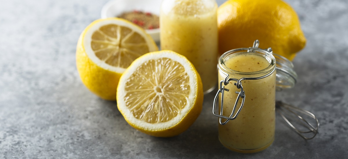 Homemade lemon vinaigrette dressing in glass jar on marble surface and surrounded by cut lemons.