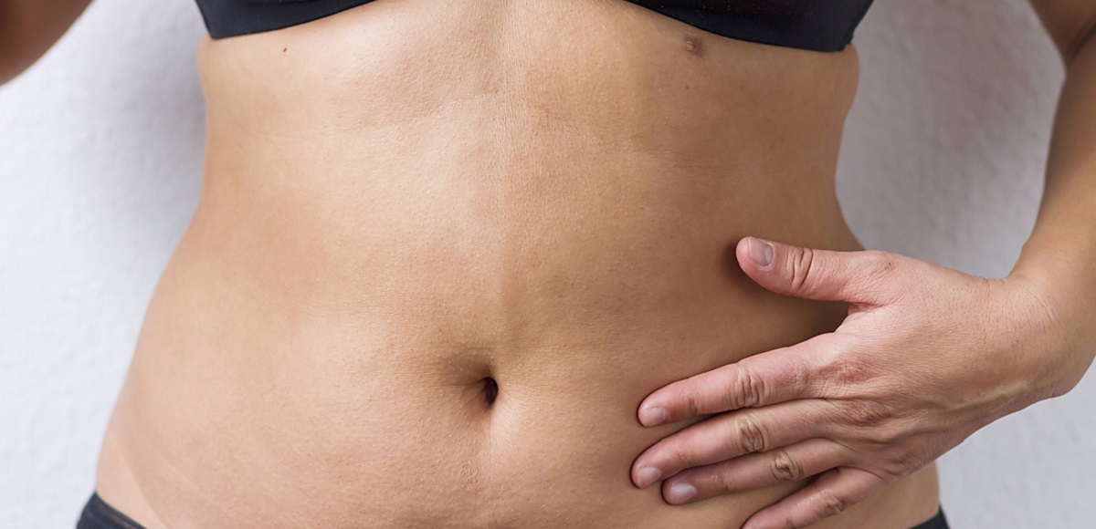 Woman wearing black undergarments with olive skin touching her stomach area.
