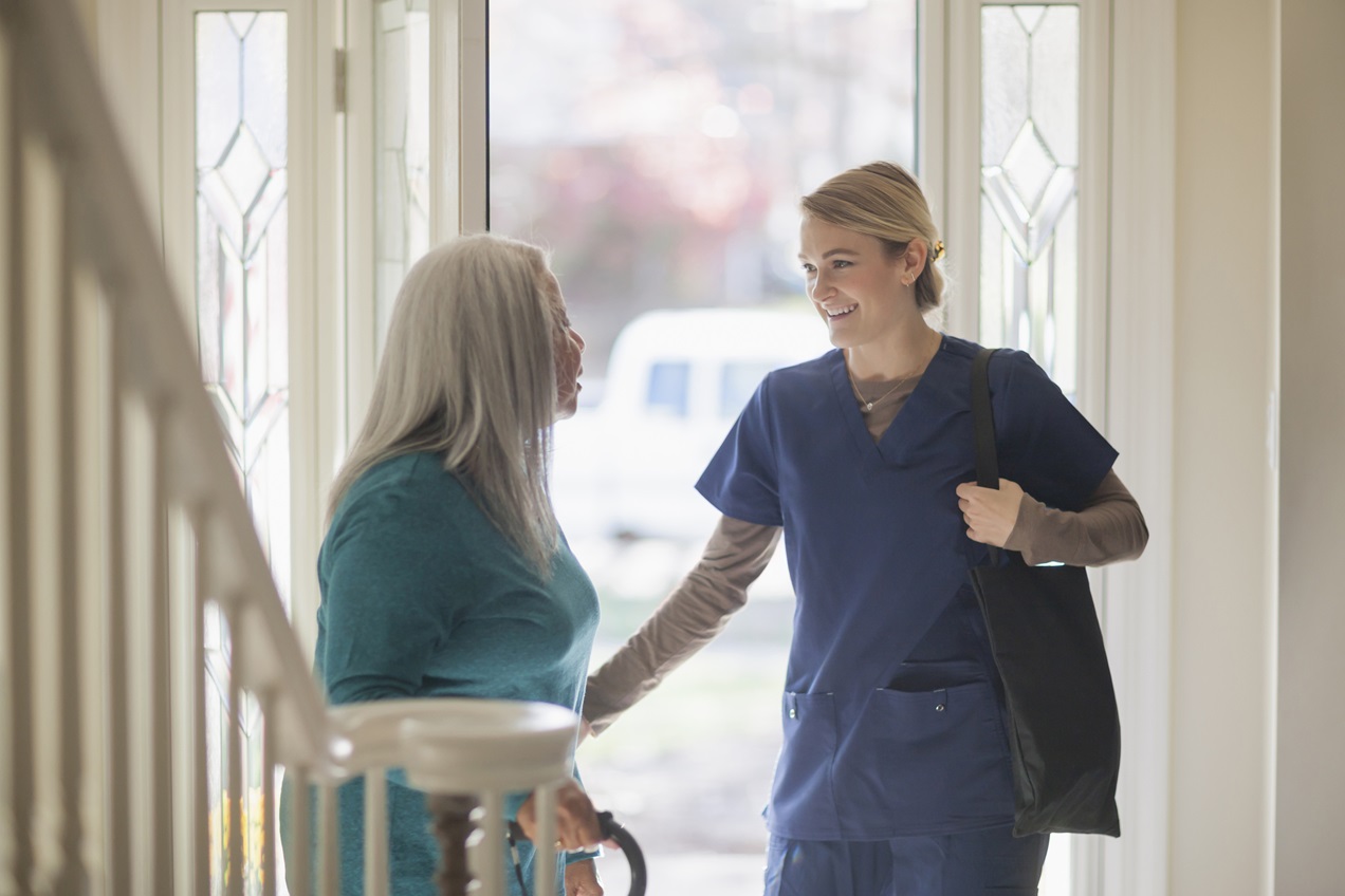 A home health care worker greets her patient in their doorway