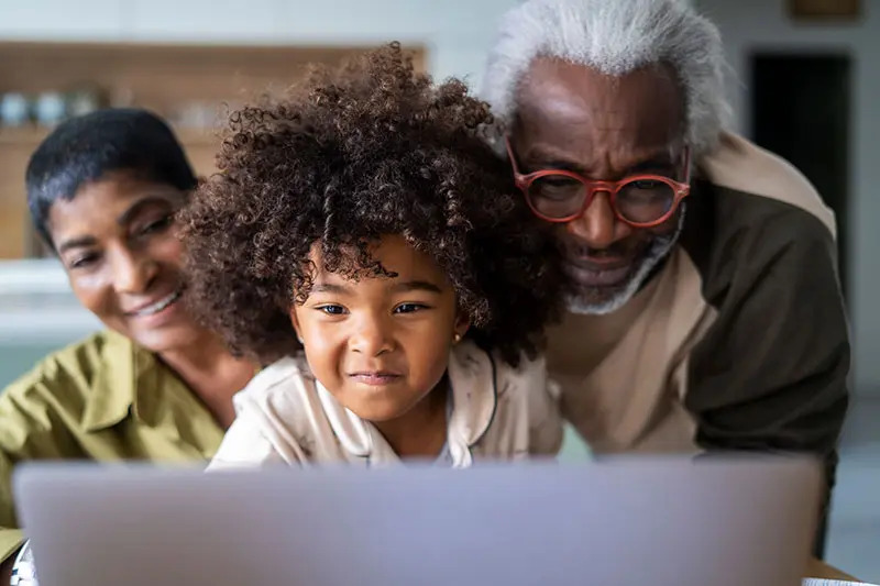 Two grandparents cuddle their granddaughter who is looking at a computer during a virtual doctor's visit