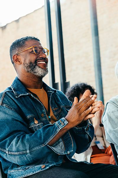 A man in a jean jacket claps at a community event